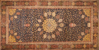 Large intricately patterned carpet in blue, burnt orange, and yellow tones. Decorative circular pattern moving out from middle. 