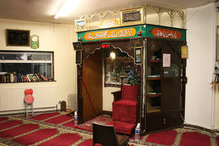 Wooden structure with a semi-circular opening, indicating the direction that Muslims should face when praying. It has a red chair and a light inside.