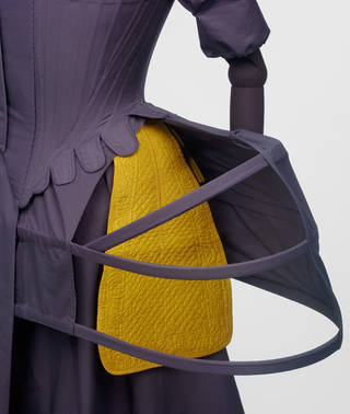 Yellow pocket displayed on a mannequin wearing a purple dress to illustrate how they were worn under garments