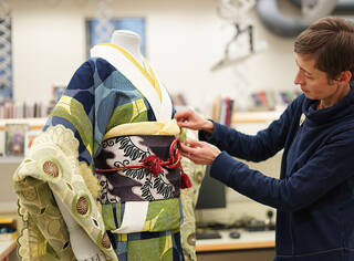 Curator mounting a green, blue, yellow and white kimono