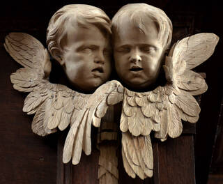 Wooden carving of two Putti heads surrounded by flowers on a dark wooden background