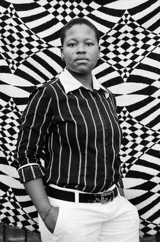 Portrait of a woman wearing black-and-white clothing against a black-and-white patterned textile background.