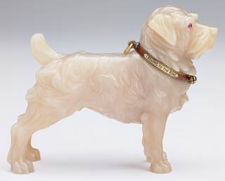 Pale cream carving of a terrier dog with pink gem eyes and a brown and gold collar inscribed 'I belong to the King'