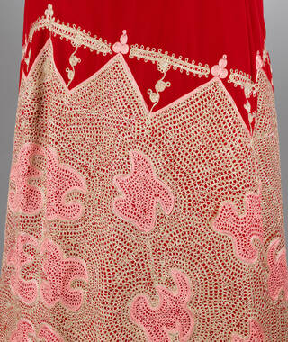 Detail of embroidery in white and pink over a red background cloth