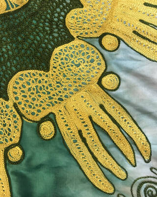 Detail of fine embroidery in greens and yellow over a lighter green background cloth