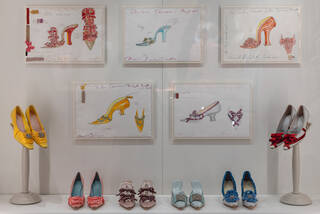 white wall with five hand-drawn designs for shoes and the five pairs of shoes displayed below