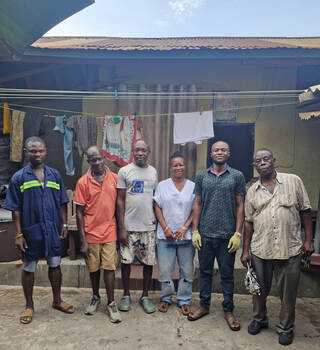 Six people standing in a row outside a single-rise building