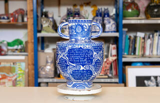Blue and white ceramic pot with detailed pattern and text decoration on a stand in a studio