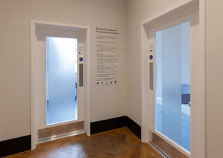 The entrances to our two quiet rooms. The doors have frosted panels to allow for private rest and reflection. Guidelines for using the room are printed on the wall between the two doors. The doors are manual and open with flat metal push plates