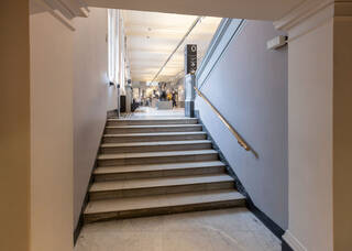 A set of eight white marble stairs leading up to the sculpture galleries. A brass handrail is on the right side of the stair, a white wall without a handrail is on the left.