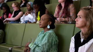 two women sat on a long green chair looking away from camera