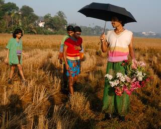 Four brightly dressed men in a field, one with a black umbrella