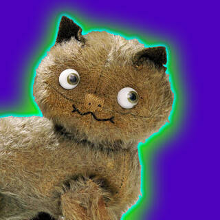 A photograph of a brown toy cat with large eyes and a smile set against a purple background with a green and blue halo.