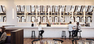 brightly lit room with bar and people sat on bar stools